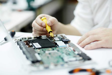 Closeup shot of unrecognizable man assembling circuit board in laptop using screwdriver and different tools on table in workshop